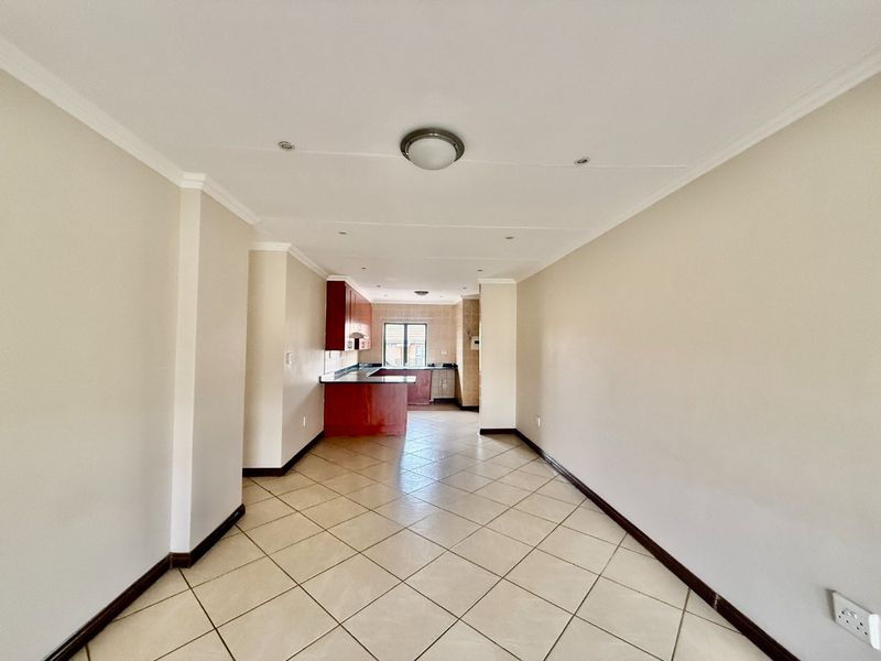 An open-plan living and kitchen area featuring tiled flooring, neutral walls, and built-in kitchen cabinetry with granite countertops.