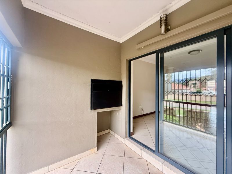 Covered balcony featuring a built-in braai, tiled flooring, and large sliding glass doors providing access to the interior living space.
