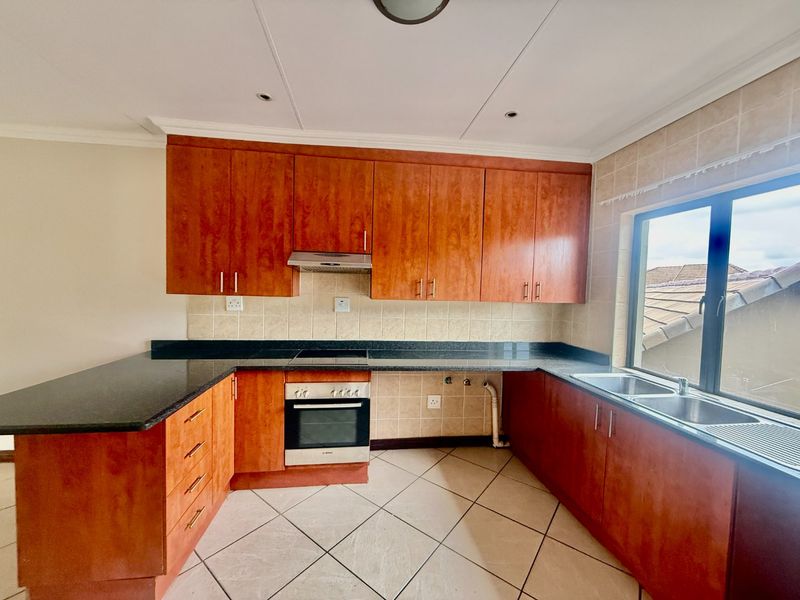 A functional kitchen featuring wooden cabinetry, granite countertops, a built-in oven, extractor fan, and a double sink with tiled flooring and backsplash.