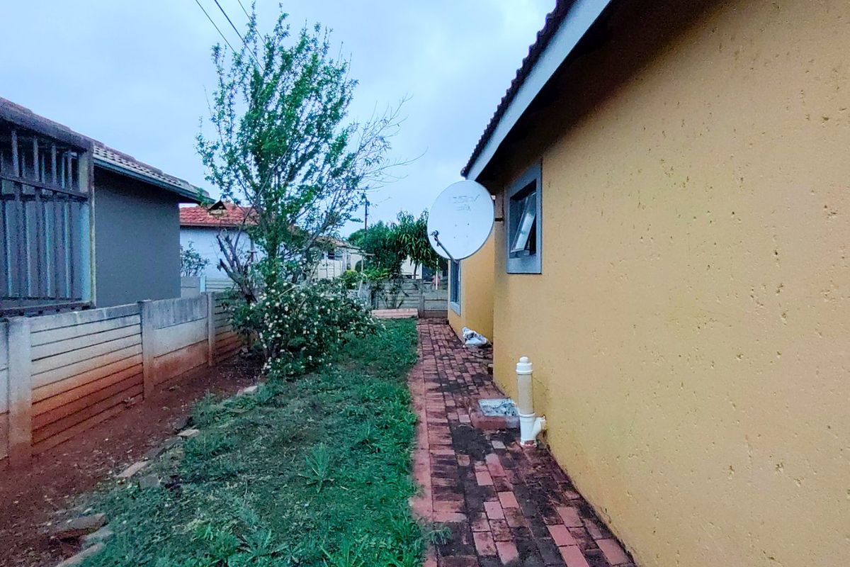 A side view of the property showing a paved walkway, boundary wall, and exterior wall with a satellite dish installation.