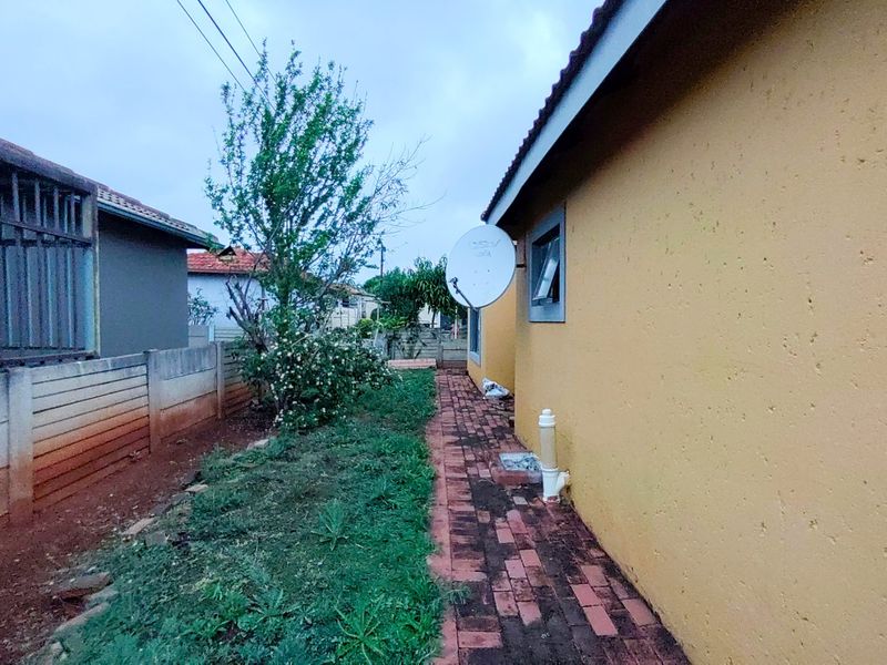 A side view of the property showing a paved walkway, boundary wall, and exterior wall with a satellite dish installation.