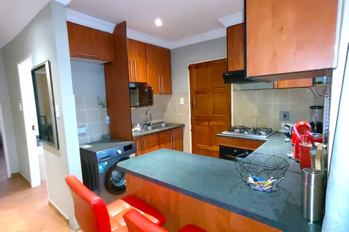 A functional kitchen featuring wooden cabinetry, dark countertops, a gas hob with extractor, and a dedicated space for a washing machine.