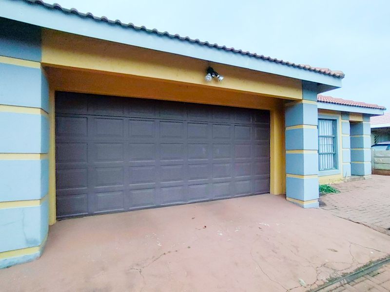 A single-car garage featuring a sectional door, tiled roof, and exterior lighting, situated on a paved driveway with visible signs of wear.