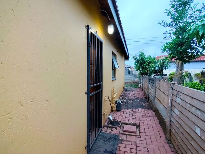 A side exterior view of the property featuring a paved walkway, security gate, and precast concrete boundary wall.