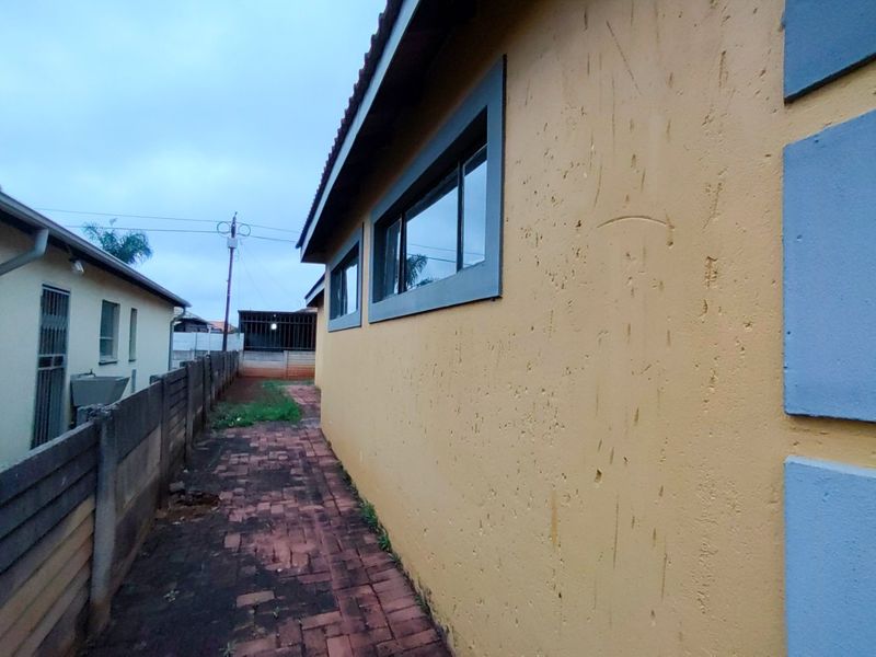Side exterior view of the property featuring a brick paved walkway, precast boundary wall, and yellow textured exterior wall finish.