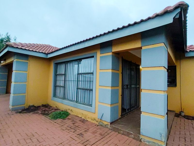 Front elevation of a house featuring a paved driveway, security gate, and tiled roof, showing signs of exterior wear and paint deterioration.