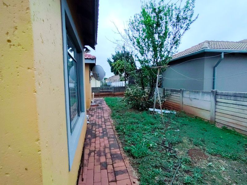 A view of the rear exterior of the property featuring a brick paved walkway, a precast boundary wall, and a small garden area.