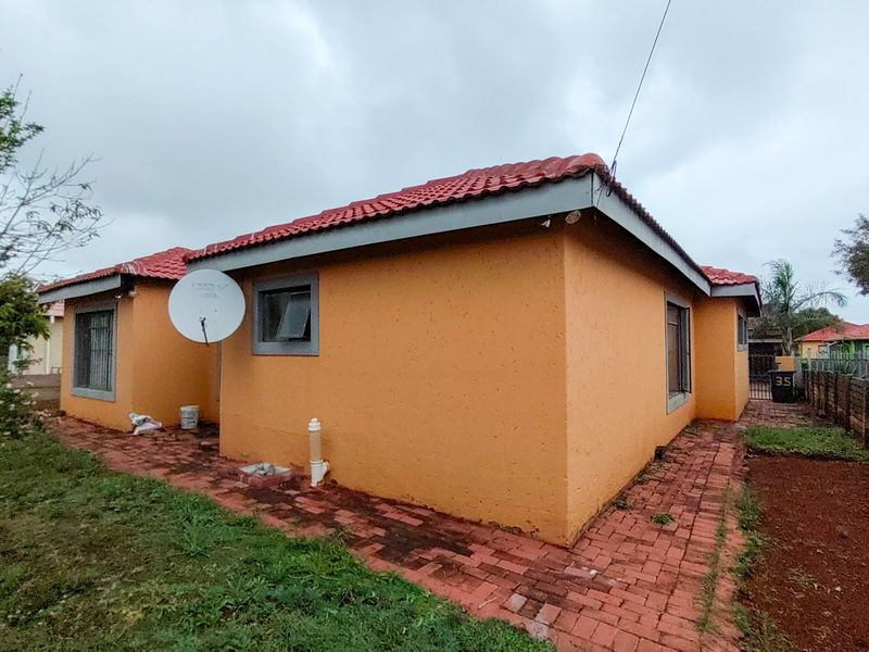 Rear view of the house featuring a tiled roof, brick paved walkway, and security bars on the windows.