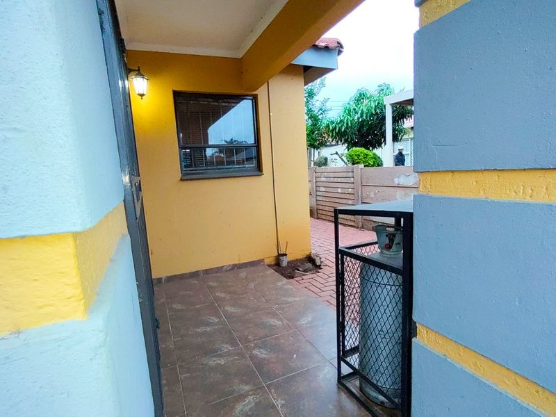 A covered patio area featuring tiled flooring, an exterior wall light, and access to a paved outdoor space.