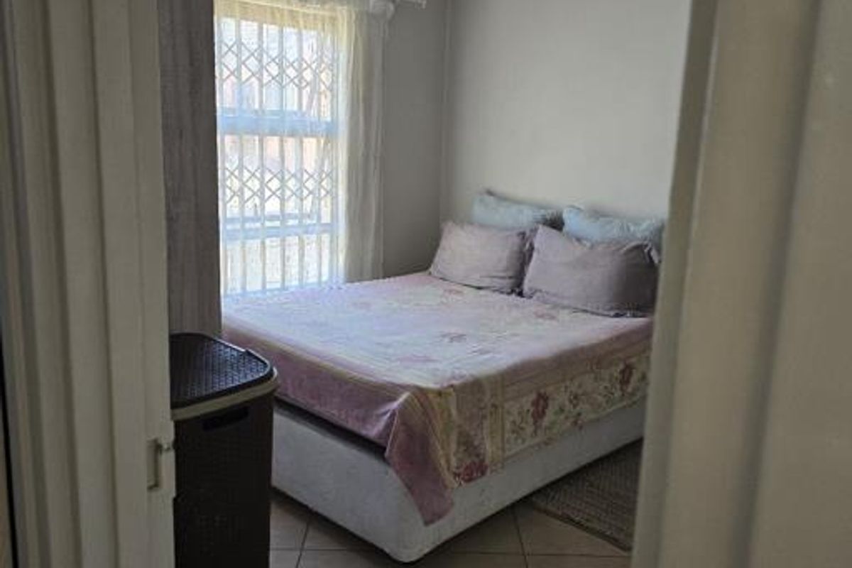 A functional bedroom featuring tiled flooring and a window fitted with a security gate, viewed from the doorway.