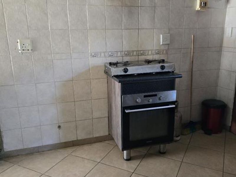 A basic kitchen area featuring tiled walls and flooring, equipped with a freestanding oven, hob, and extractor fan.