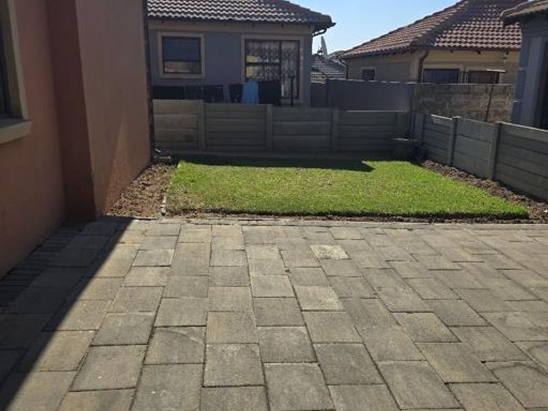 A rear exterior view featuring a paved patio area, a small lawn, and precast concrete boundary walls.