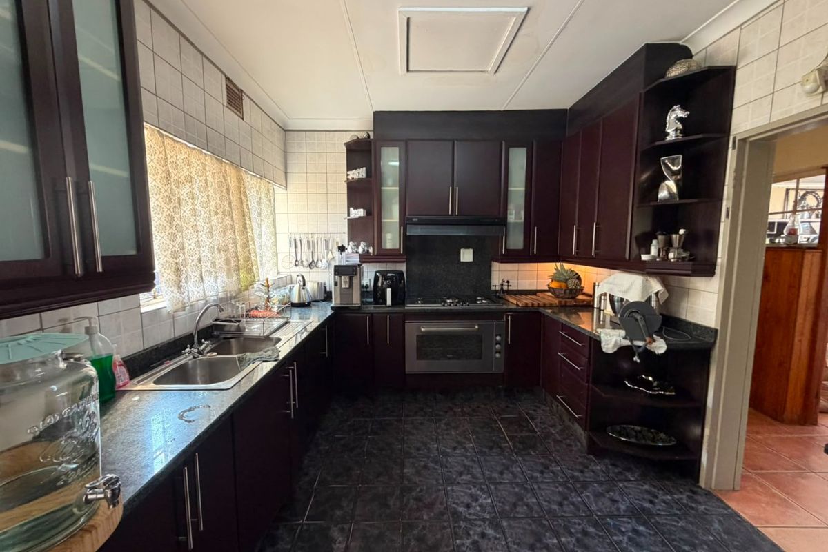 A functional kitchen featuring dark wood cabinetry, granite countertops, a built-in oven with extractor fan, and tiled finishes throughout.