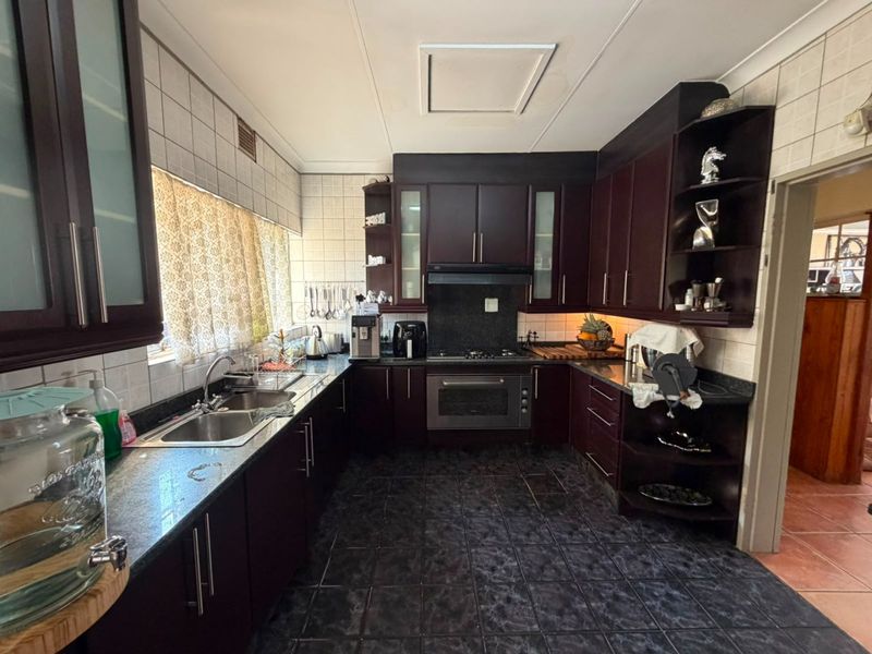 A functional kitchen featuring dark wood cabinetry, granite countertops, a built-in oven with extractor fan, and tiled finishes throughout.
