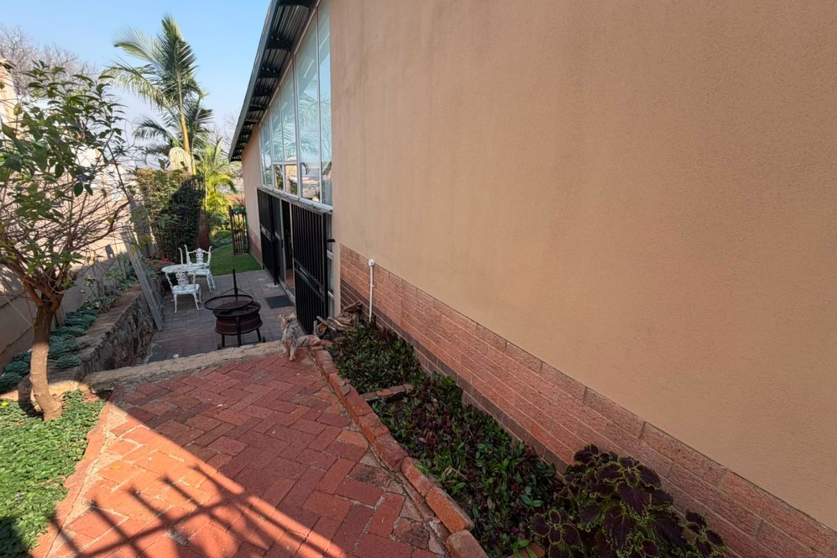 A rear exterior view showing a brick paved walkway, a retaining wall, and access to the home via sliding glass doors with security gates.
