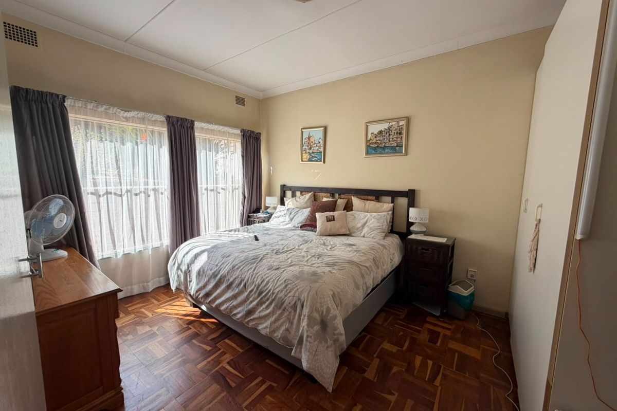 A well-proportioned bedroom featuring classic parquet flooring, built-in storage, and large windows that provide ample natural light.