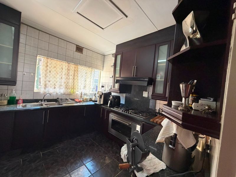 A functional kitchen featuring dark wood cabinetry, granite countertops, a gas hob, and a built-in oven, with tiled finishes throughout.