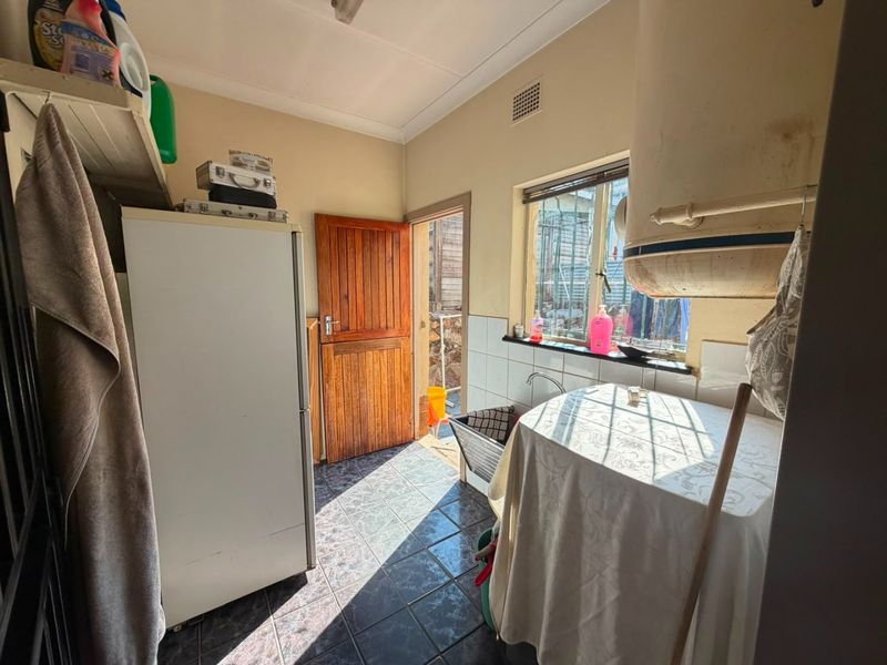 A functional laundry area featuring tiled flooring, a sink, and direct access to the exterior through a timber door.