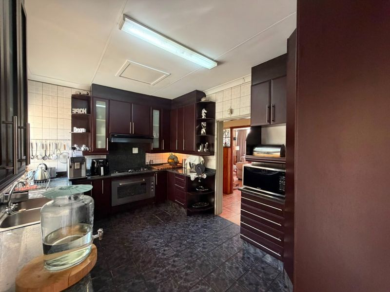 A functional kitchen featuring dark wood cabinetry, granite countertops, built-in oven, gas hob, and tiled finishes throughout.