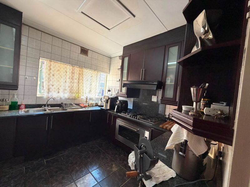 A functional kitchen featuring dark wood cabinetry, granite countertops, built-in oven, gas hob, and tiled finishes, with visible ceiling water staining.