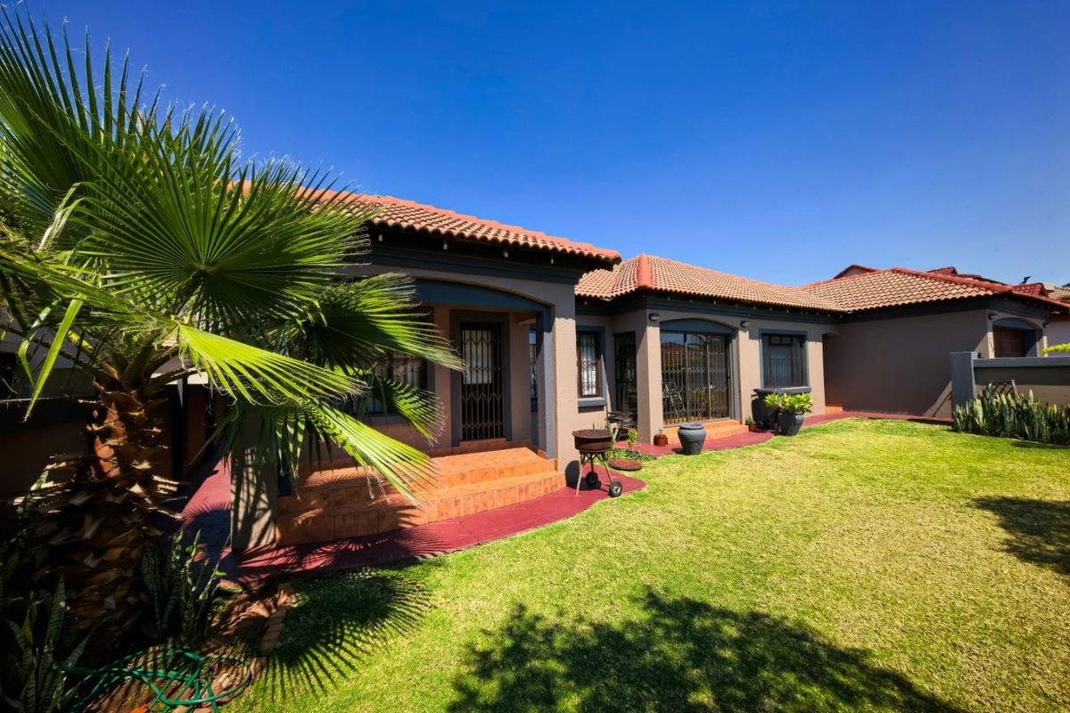 A well-maintained rear exterior view featuring a covered patio, terracotta tiled roof, and a neat garden area with paved walkways.