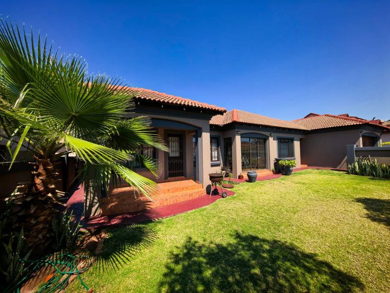 A well-maintained rear exterior view featuring a covered patio, terracotta tiled roof, and a neat garden area with paved walkways.
