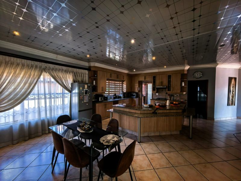 Open-plan kitchen and dining area featuring granite countertops, wooden cabinetry, and distinctive decorative ceiling panels with tiled flooring throughout.