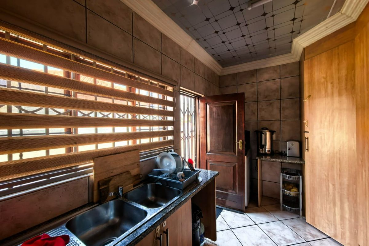 Functional kitchen featuring double stainless steel sinks, granite countertops, built-in wooden cabinetry, and tiled finishes throughout.