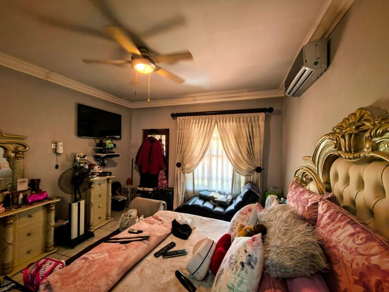 A bedroom featuring a ceiling fan, split-system air conditioning unit, and crown molding, with tiled flooring throughout.