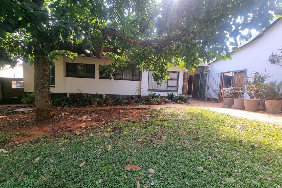 A rear garden view featuring a paved patio area, mature tree, and lawn, providing a private outdoor space adjacent to the house.