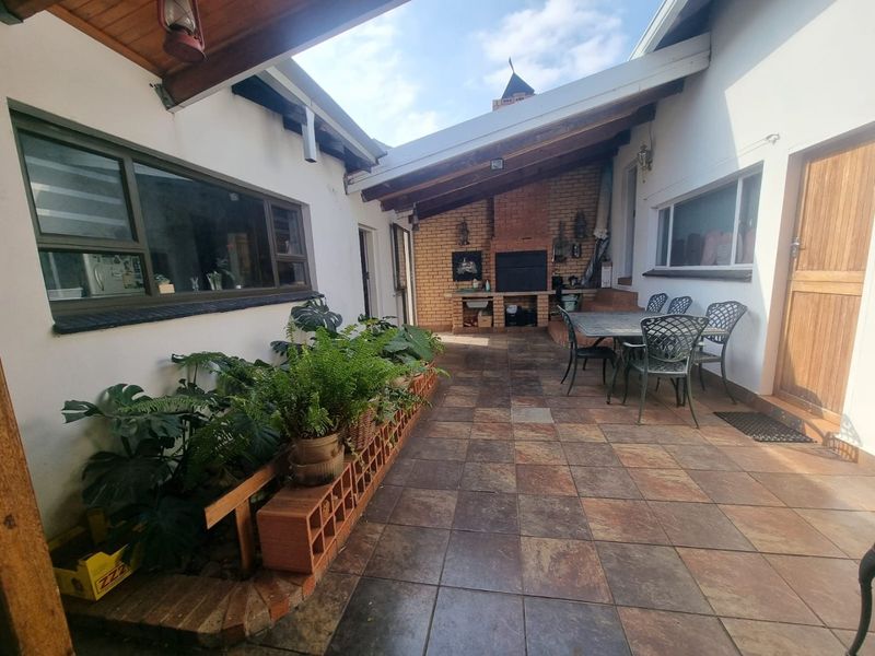 Covered outdoor patio area featuring a built-in brick braai, tiled flooring, and exposed timber ceiling beams, ideal for outdoor entertaining.