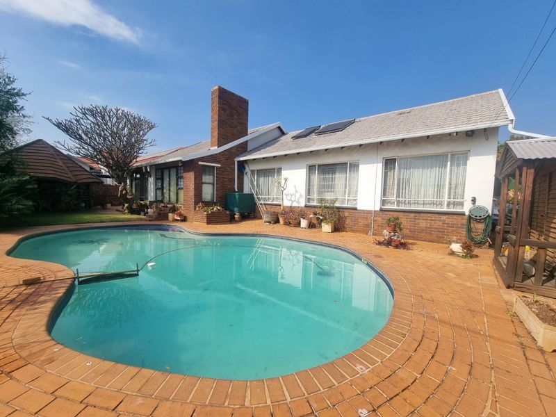 Rear exterior view featuring a swimming pool, brick paved patio area, and a house with a brick chimney and solar panels.