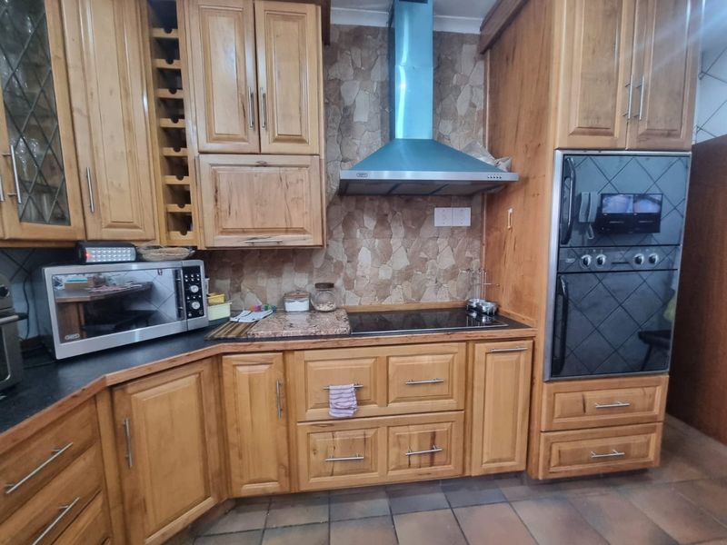 A traditional kitchen featuring wooden cabinetry, a stone-look backsplash, built-in oven, electric hob, and extractor fan with tiled flooring.
