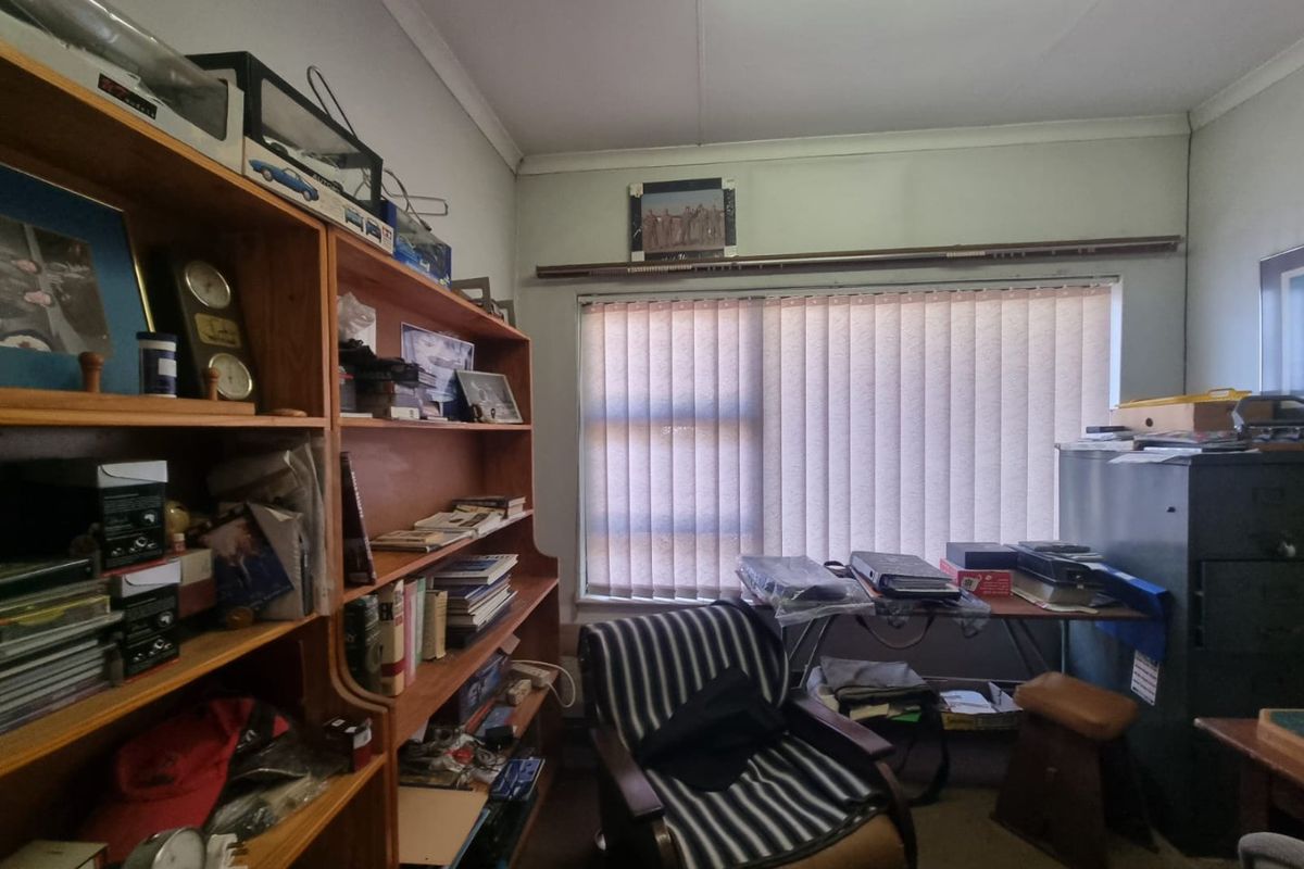 A bedroom space featuring vertical blinds and standard ceiling cornicing, currently utilized as a home office or storage area.