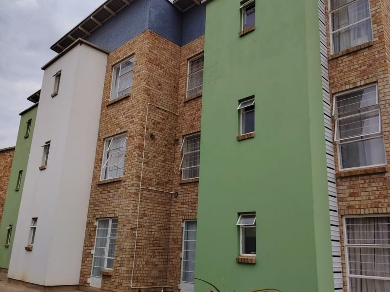 Exterior view of a multi-story apartment building featuring a combination of brickwork, painted plaster sections, and casement windows with a paved ground-level walkway.