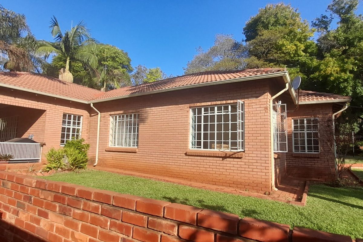 Rear view of a classic brick farmhouse featuring a tiled roof, security-barred windows, and a covered patio overlooking the garden.
