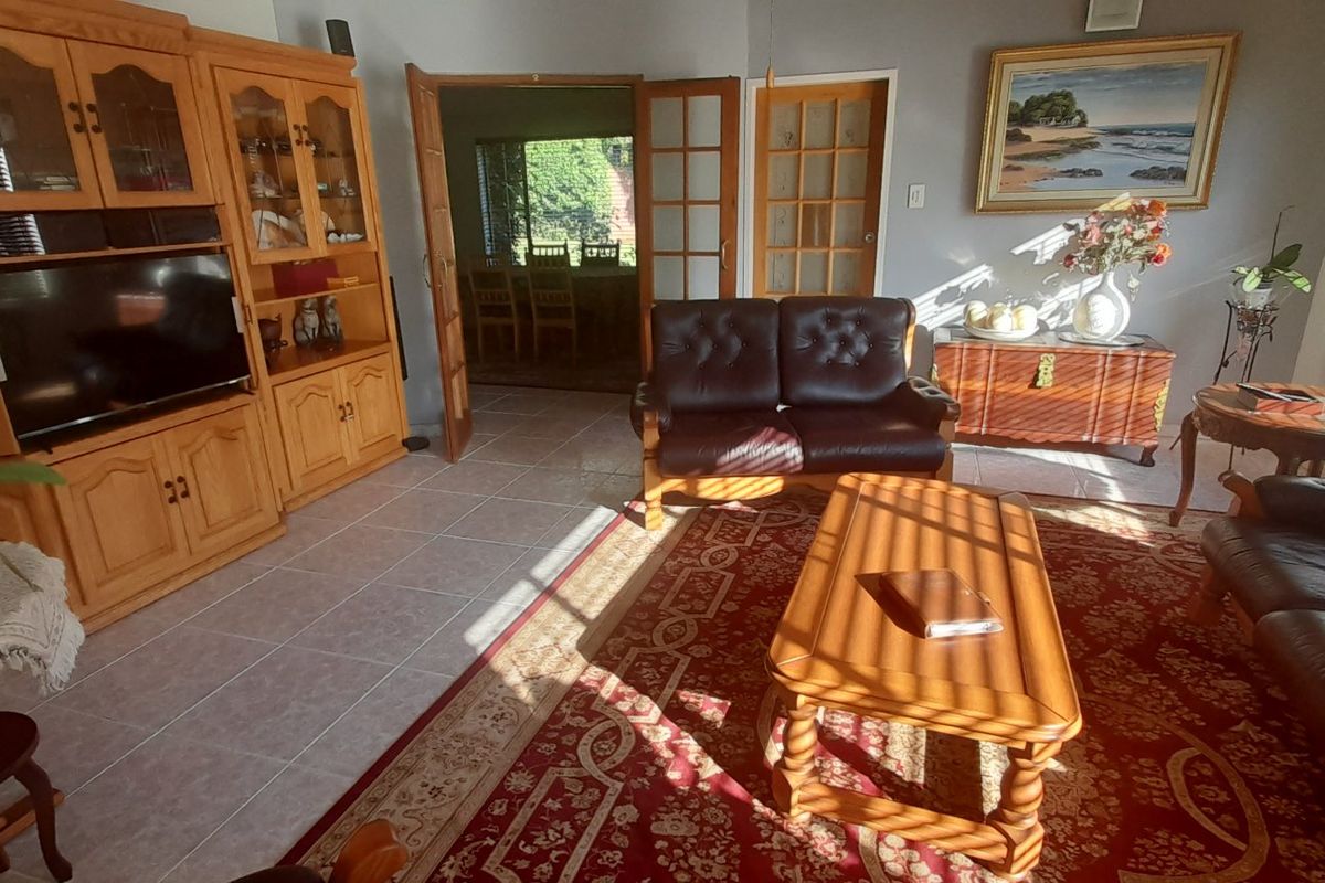 A spacious living room featuring tiled flooring, natural light through venetian blinds, and double french doors leading to an adjacent dining area.