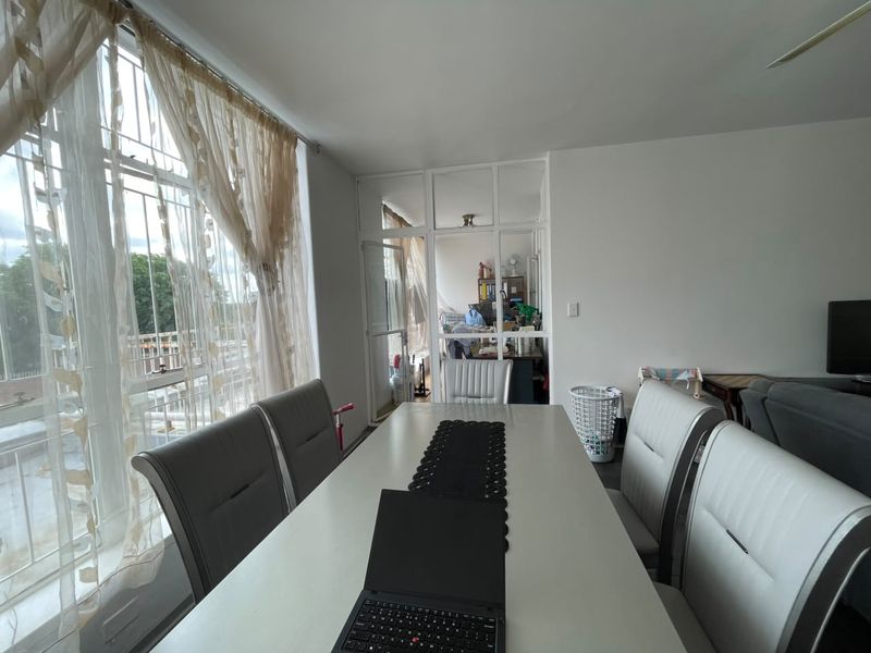 Open plan living and dining area featuring large windows with security bars and a glass partition wall separating the adjacent space.