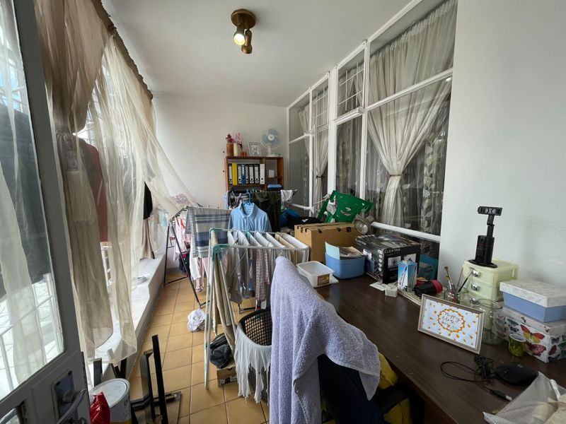 A functional enclosed balcony or sunroom featuring tiled flooring and large windows, currently utilized as a multi-purpose utility and workspace area.