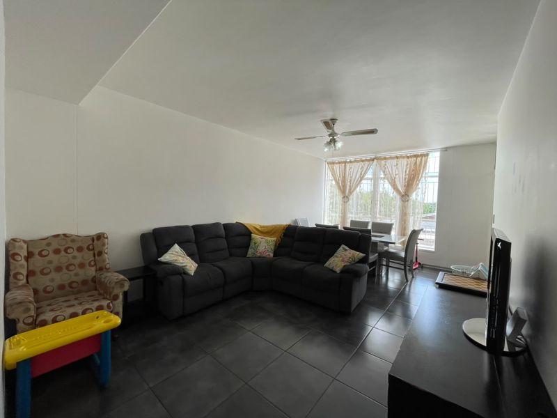 Open plan living and dining area featuring dark tiled flooring, a ceiling fan, and large windows allowing for natural light.