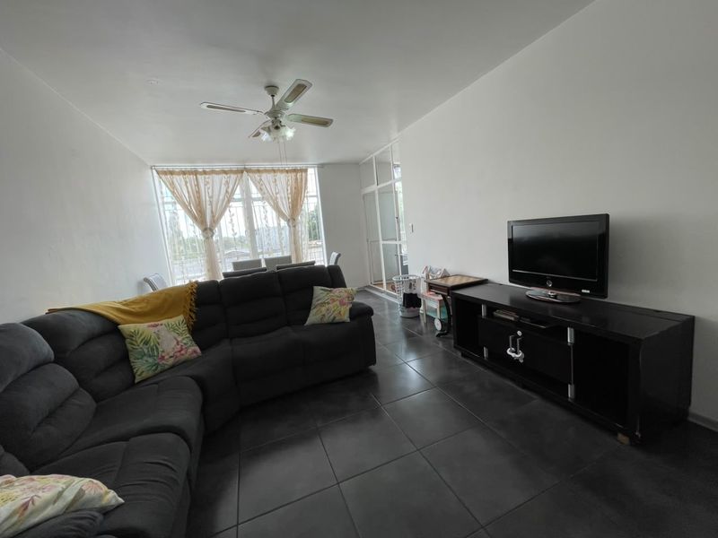 A living room featuring dark tiled flooring, a ceiling fan, and large windows providing natural light, with access to an adjacent balcony area.