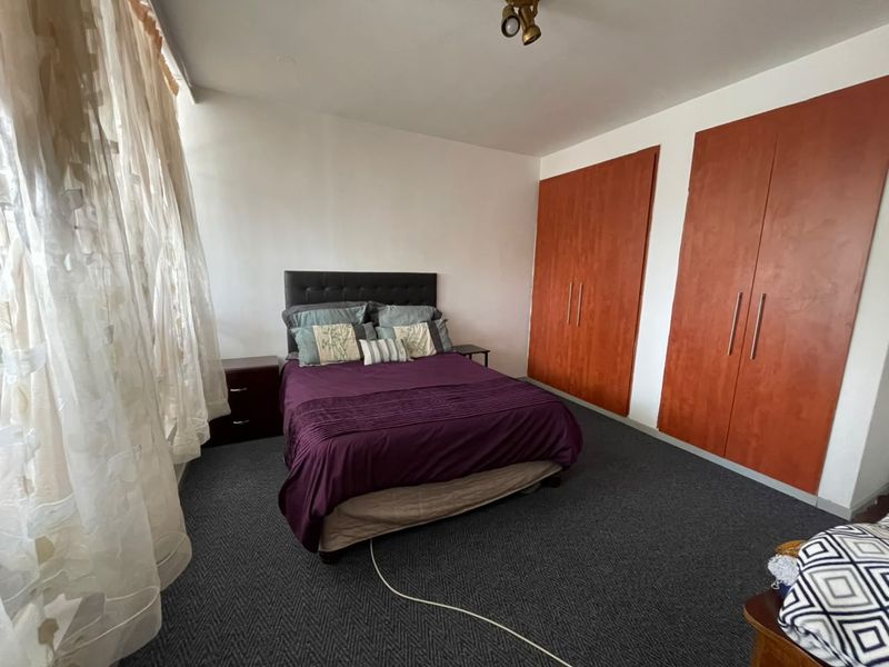 A bedroom featuring dark carpeted flooring, built-in wooden cupboards, and a ceiling light fixture, offering a functional space with neutral wall finishes.