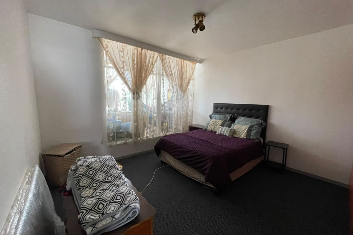 A standard bedroom featuring dark carpeting and a large window with natural light, providing a functional space for rest.