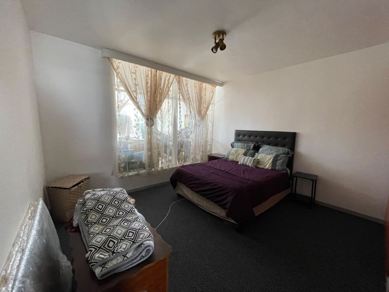 A standard bedroom featuring dark carpeting and a large window with natural light, providing a functional space for rest.