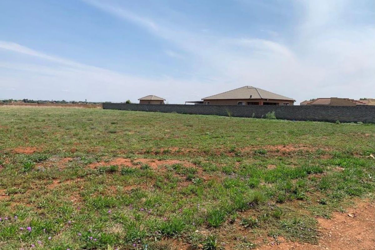 A vacant residential plot featuring natural grass cover and a perimeter boundary wall, offering a clear space for future development.