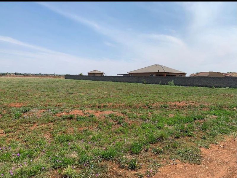 A vacant residential plot featuring natural grass cover and a perimeter boundary wall, offering a clear space for future development.