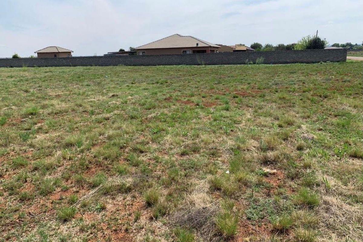 A vacant residential plot featuring natural grass cover and a perimeter boundary wall, offering a clear space for future development.