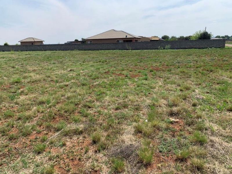 A vacant residential plot featuring natural grass cover and a perimeter boundary wall, offering a clear space for future development.