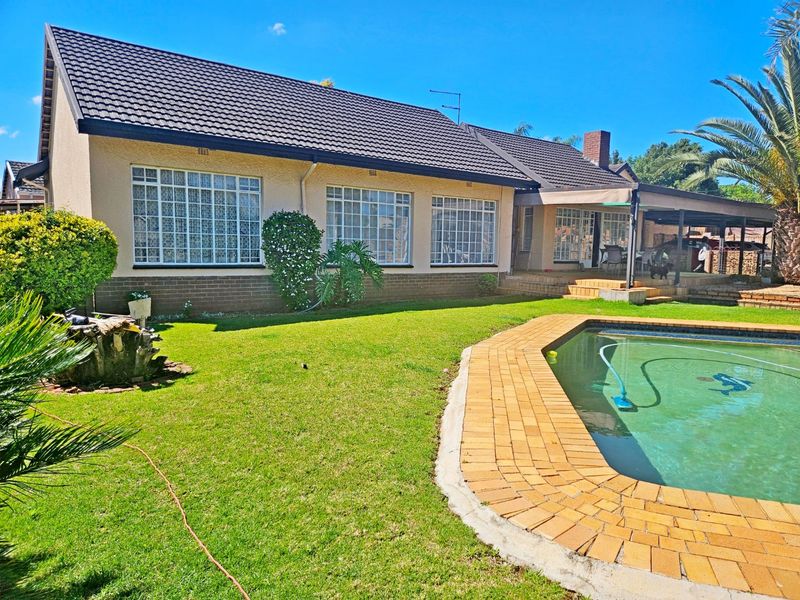 Rear view of the house featuring a tiled roof, brick facade, covered patio area, and a swimming pool with brick coping.