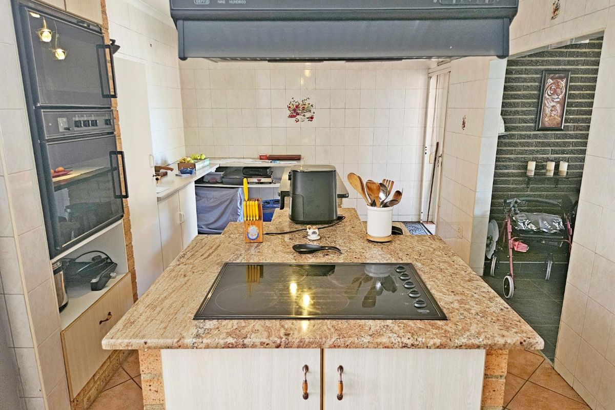 A functional kitchen featuring a central granite island with a built-in hob, double wall oven, and tiled finishes throughout.